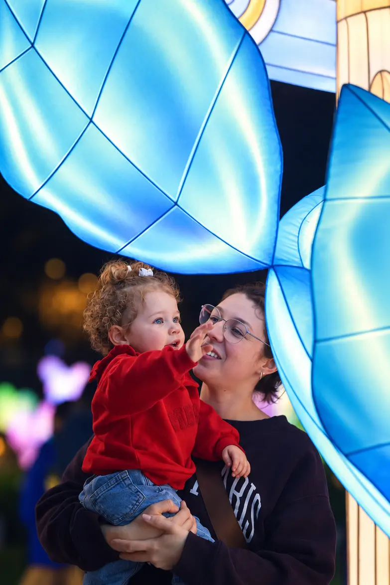 A parent holding a toddler who reaches up toward glowing blue lanterns